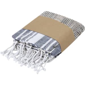 A folded set of striped towels in blue and white, wrapped with a brown paper band. The towels feature tassels.