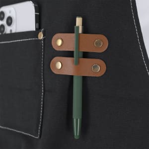 A black Fonor apron with a brown leather strap holding a green pen, featuring a pocket for a smartphone.