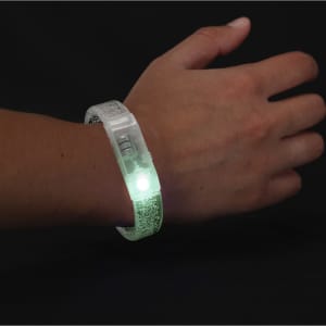 A glowing green bracelet is worn on a wrist, featuring a textured design and an embedded light.