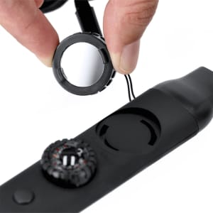 A black survival whistle is held by a hand, showcasing a removable cap and a threaded attachment point.
