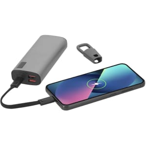 A grey charging cable connected to a smartphone, with a portable charger beside it. The setup includes a keychain attachment.