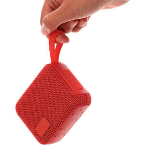 A red portable speaker with a handle is being held by a hand. The speaker has a textured surface and a button on the side.