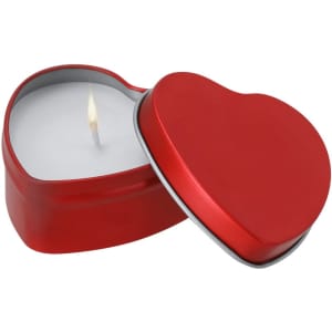 A heart-shaped red tin containing a white fragrant candle, with a single flame flickering.