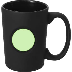 A coffee mug in matte black with a circular area for branding or personalisation in light green.