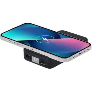 A black power bank with a phone charging wirelessly on top, featuring multiple USB ports and a logo.