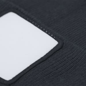A dark beanie featuring a white rectangular patch, with a textured fabric design. It includes a logo or branding.