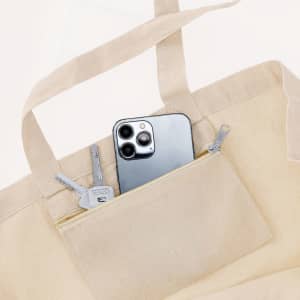 A beige tote bag with a smartphone and keys visible in its exterior pocket. The bag features zippers and sturdy handles.