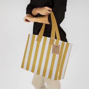A tote bag with gold and white stripes, featuring a logo and medium-length straps.