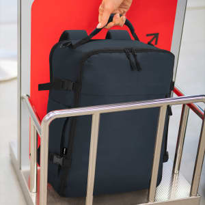 A dark navy backpack with adjustable straps is being held by a person at a security checkpoint.
