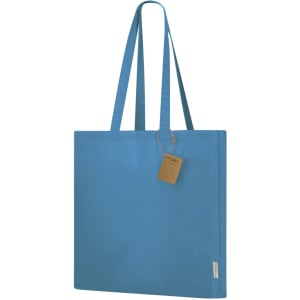 A blue tote bag with long handles and a tag attached, featuring a simple design. It has a logo on one side.