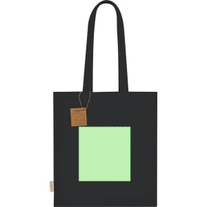 A black tote bag featuring a square green panel and a tag attached. It has sturdy handles for carrying.