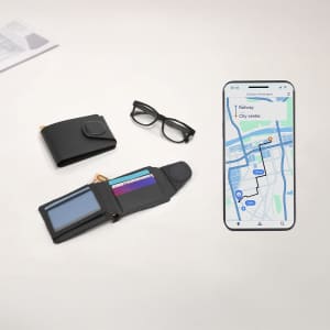 A black Nairobix Tracker Card Holder Wallet is displayed open, showing card slots, alongside glasses and a phone with a map.