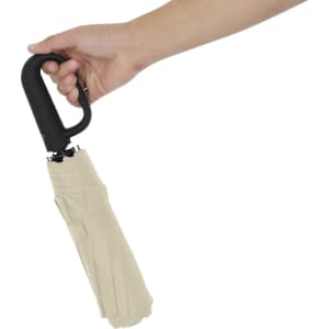 A beige umbrella with a black handle, held in a hand, showcasing its compact design.
