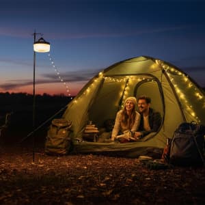 A tent illuminated by fairy lights, with a couple sitting inside, enjoying the evening. Various backpacks are nearby.