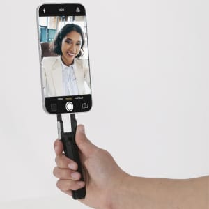 A black phone holder featuring a grip, supporting a smartphone in a vertical position. The phone displays a selfie.