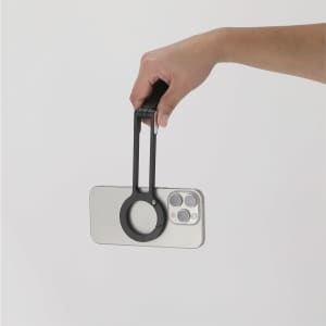 A black phone holder is being held by a hand, featuring a circular grip for easy handling.