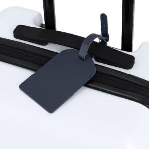 A navy blue luggage tag attached to a white suitcase, featuring a simple design and a logo.
