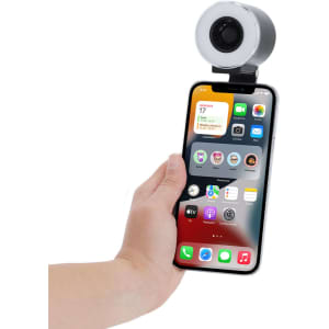 A phone with a silver Tangix Fan Ring Light attached to its top, held in a hand.