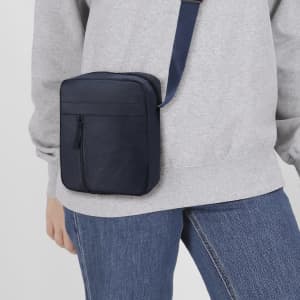 A navy shoulder bag with a zippered front pocket, worn across the body against a light grey sweatshirt.