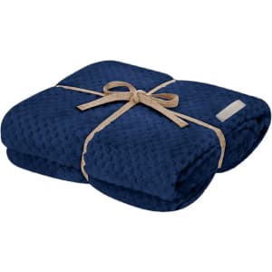 A navy blue blanket folded neatly and tied with a ribbon, featuring a small branding label.