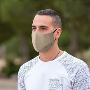 A reusable hygienic mask in a beige colour, worn by a person outdoors with greenery in the background.