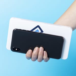 A hand holds a white multipurpose bag with a logo, revealing a black smartphone partially inside.