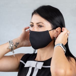 A woman adjusts a black reusable hygienic mask on her face. The mask is simple and sleek in design.