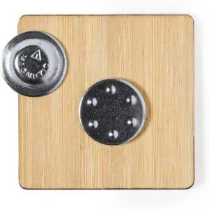 A square lapel pin with a metallic backing, displayed on a wooden surface. The pin features a simple design.