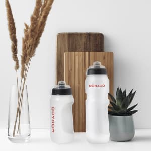 A drink bottle set in clear and white with black lids, alongside a plant and decorative items. Features branding.