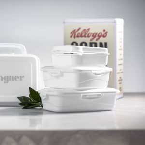 A white Zenex lunch box set featuring three containers stacked on a surface, with a drink bottle and a cereal box in the background.
