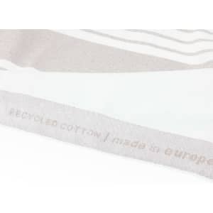 A soft grey and cream striped towel made of recycled cotton, featuring a branding label on one edge.