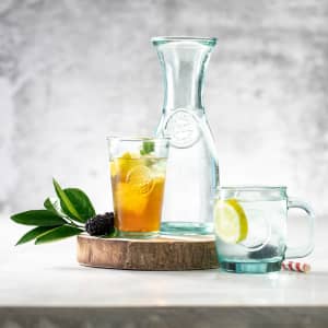 A drinkware display featuring a clear glass jug, a glass with a fruit-infused beverage, and a mug with a slice of lemon.