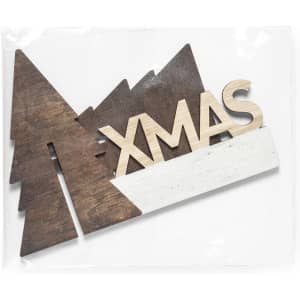 A decorative wooden "XMAS" ornament with brown trees and a white base, packaged for sale.