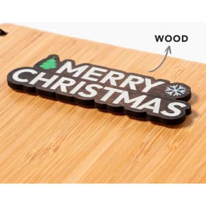 A wooden tag featuring the words "Merry Christmas," displayed on a light bamboo surface.