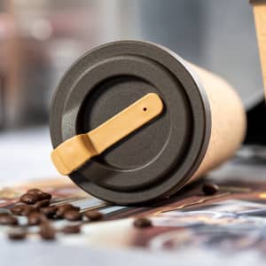 An insulated travel mug with a brown and black design, featuring a flip-top lid and a logo.