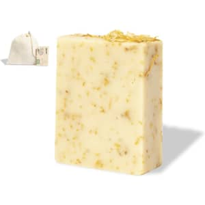 A block of soap with a creamy colour and dried flowers embedded, alongside a small fabric bag.