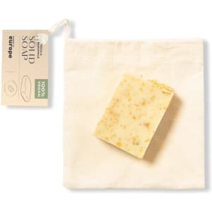Solid soap featuring a creamy hue with specks, resting on a natural fabric pouch. The pouch includes a tag.