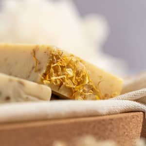 A close-up of natural soap bars with dried flowers, set on a neutral background. The soap has a creamy colour.