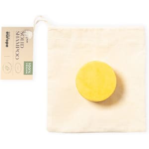 A round yellow solid shampoo bar placed in a natural fabric pouch, featuring a simple logo.