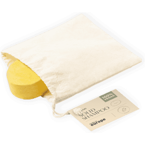A yellow solid shampoo bar with a natural fabric pouch and a labelled card beneath it. The product has a logo.