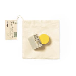 A set of handmade soap bars in various colours, including yellow and white, packaged in a natural fabric pouch.