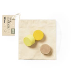 Three solid shampoo bars in yellow and brown, packaged in a natural fabric pouch with a tag.
