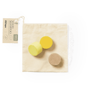 A set of three solid shampoo bars in yellow and brown, packaged in a natural fabric pouch.