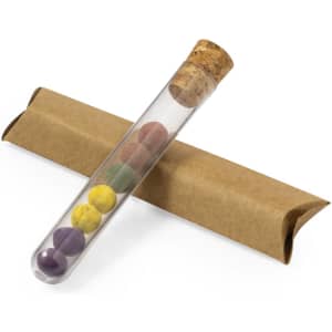 A glass test tube with a cork stopper holds colourful seed bonbons, placed on a brown paper packaging.