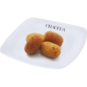 A white plate with a logo features four golden-brown croquettes arranged neatly.