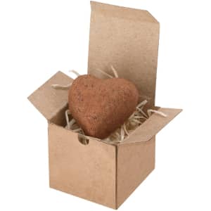 A heart-shaped chocolate in a small brown box filled with straw-like packaging. The box is partially open.