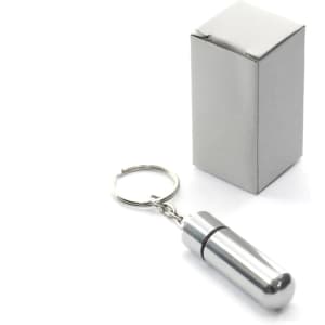 A silver keyring pillbox in the shape of a capsule, next to a plain white box.