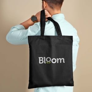 A black tote bag featuring a logo, held by a person wearing a light blue shirt.
