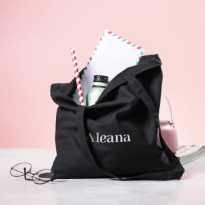 A black tote bag filled with a drink bottle, letters, and a straw, alongside a pair of glasses.