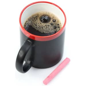 A black coffee mug with a red rim, filled with coffee and accompanied by a pink chalk piece.